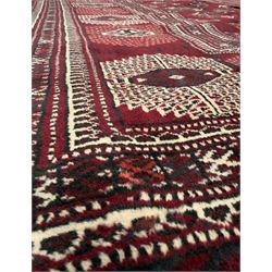 Northeastern Persian Yamut  hand-knotted carpet, the rich burgundy field with repeating rows of stepped gul motifs in cream and black, enclosed by multiple linear and geometric borders with hooked motifs and diamond medallions