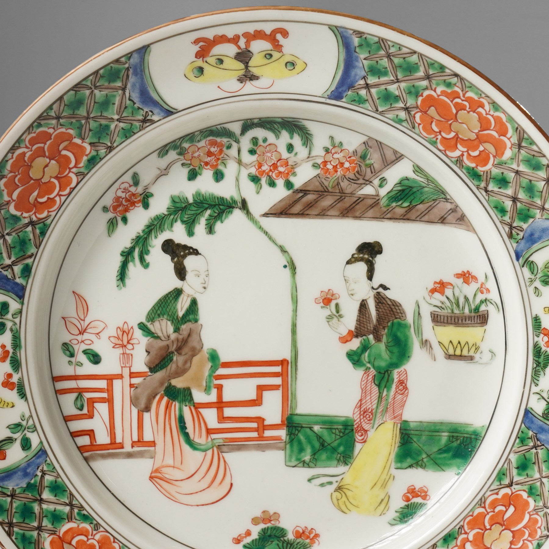 Chinese famille verte plate, painted with two ladies in a garden terrace setting, the border with butterfly and insect vignettes, D23cm 