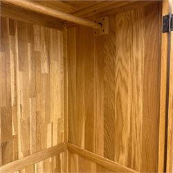 Modern light oak double wardrobe, with twin panelled doors enclosing hanging rail and full-height interior, above a deep lower drawer with recessed handle, shaped stiles