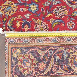 Central Persian Kashan hand-knotted rug, crimson field, profusely decorated with scrolling vines and palmettes, floral sprays around an ivory and indigo lobbed medallion enclosed by spandrels within an indigo border of arabesques between multiple guard stripes  