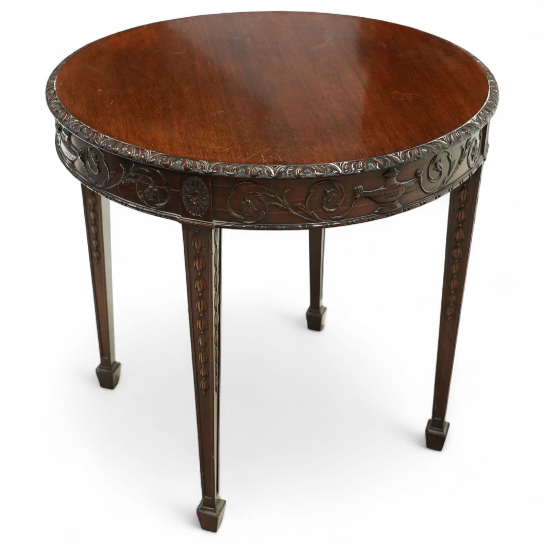 Early 20th century mahogany circular centre table in the Adams style, the moulded frieze carved with scrolling foliage and urn motifs between rosettes, raised on square tapering legs with carved husk decoration and terminating in spade feet