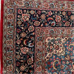 Meshed Persian rug, red, indigo, and teal background with repeating floral vine around a symmetrical floral medallion with bold palmettes, central ivory radiating floral centrepiece, and spandrels, indigo and teal border of delicate scrolling palmette and leafy floral vines