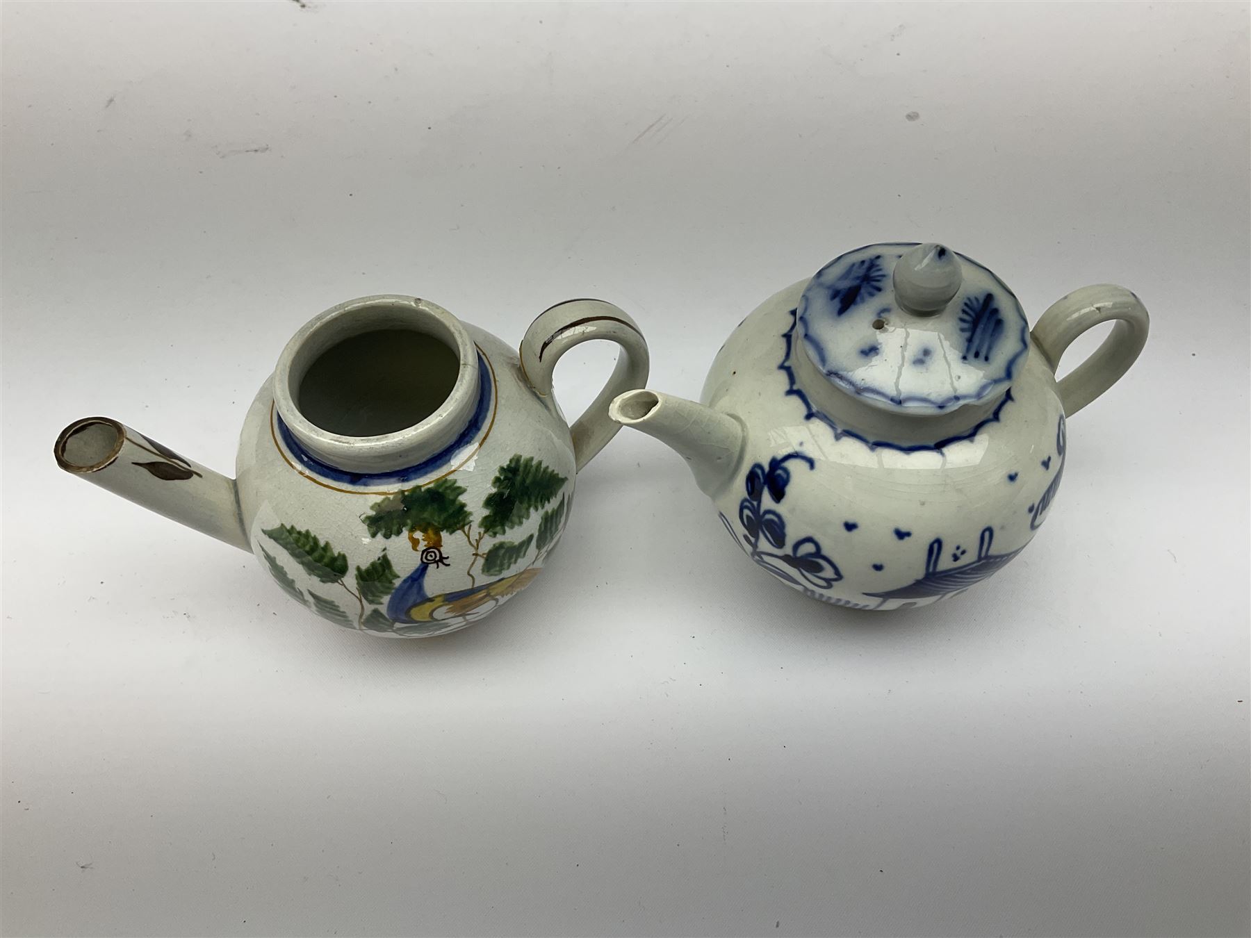 Two 18th century miniature or toy pearlware teapots, the first example lacking cover decorated with an exotic bird, the second with cover painted in underglaze blue with hut and fence, second example approximately H8cm
