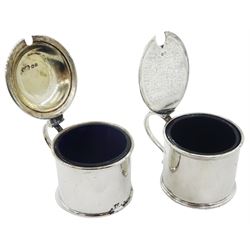 Two early 20th century silver mustard pot and covers, each of plain drum form, the first example with domed cover, hallmarked Reid & Sons, London 1927, the second with scroll handle, hallmarked Crichton Brothers, London 1935, each with blue glass liner, each approximately H6cm, approximate total silver weight 5.98 ozt (186.2 grams)
