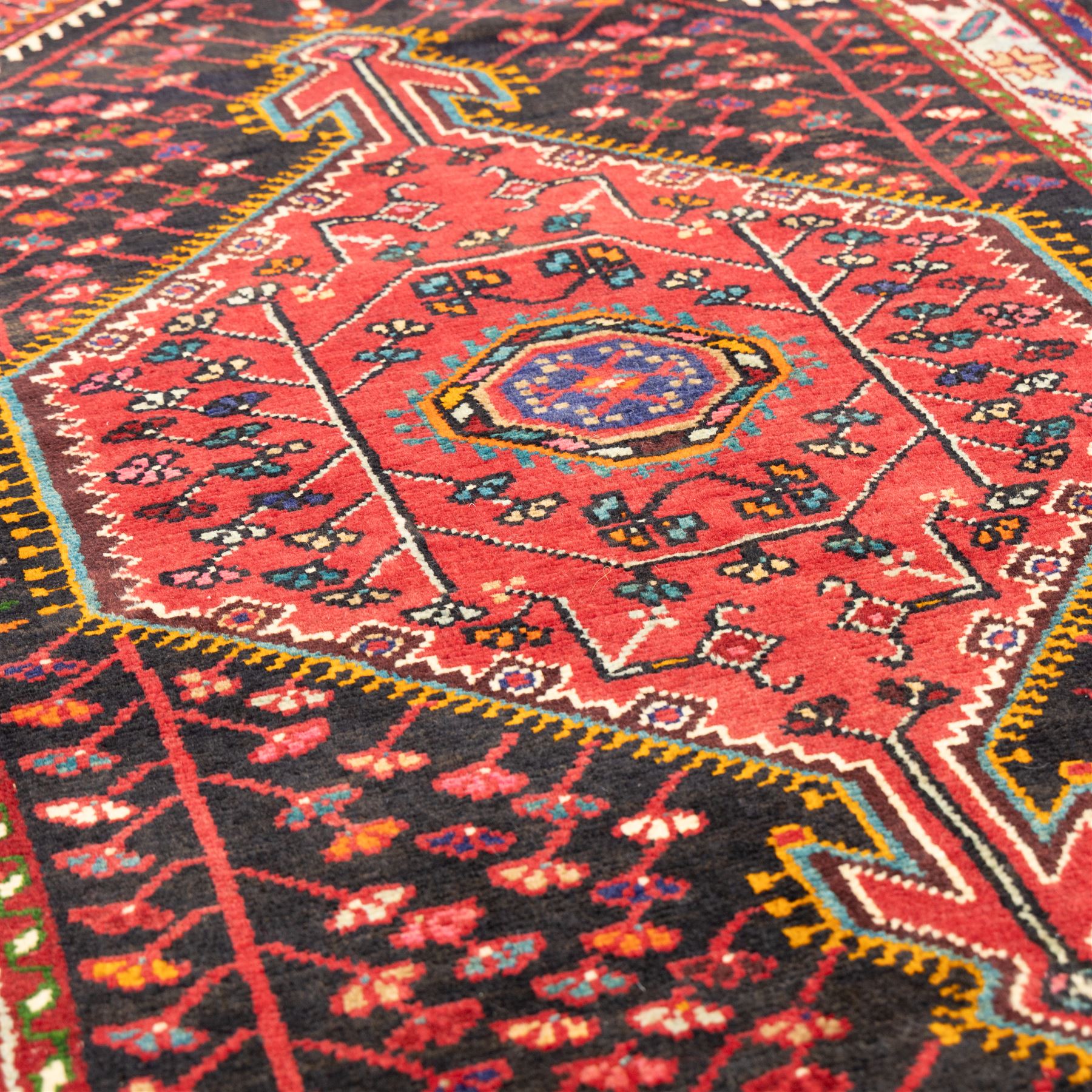 North west Persian Koliahee hand-knotted rug, central magenta field with elongated hexagonal medallion and arrow-shaped pendants over a dark lozenge-filled panels and stepped spandrels filled with boteh and floral motifs, corner square and cruciform devices within a pale olive border of stylized rosettes and angular vines between narrow guard stripes 