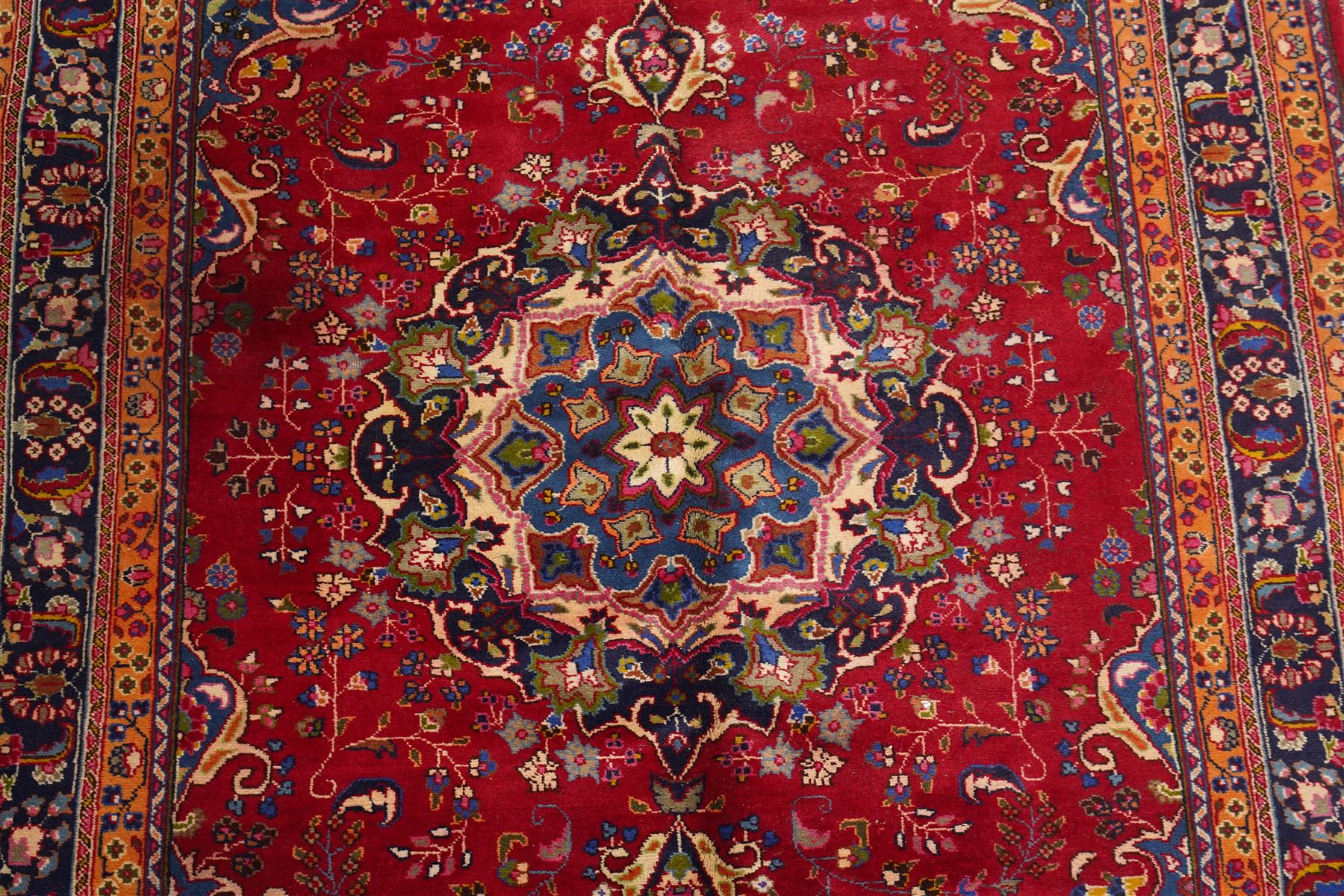 Persian Kashan hand-knotted rug, madder red ground centred by circular floral medallion with pendants, surrounded by scrolling vines, palmettes and flowerheads, dark navy spandrels, enclosed by dark navy floral border with multiple guard stripes