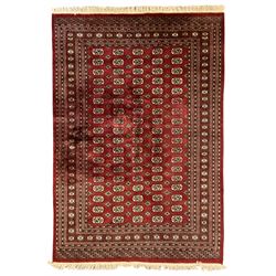 Pakistani Bokhara red ground rug, the field decorated with repeating Gul motifs and lozenges, the multi-band border with stylised plant motifs with dark indigo outlines