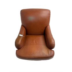 Traditional shaped armchair, scrolled back, upholstered in tan leather, raised on turned supports with brass cups and castors
