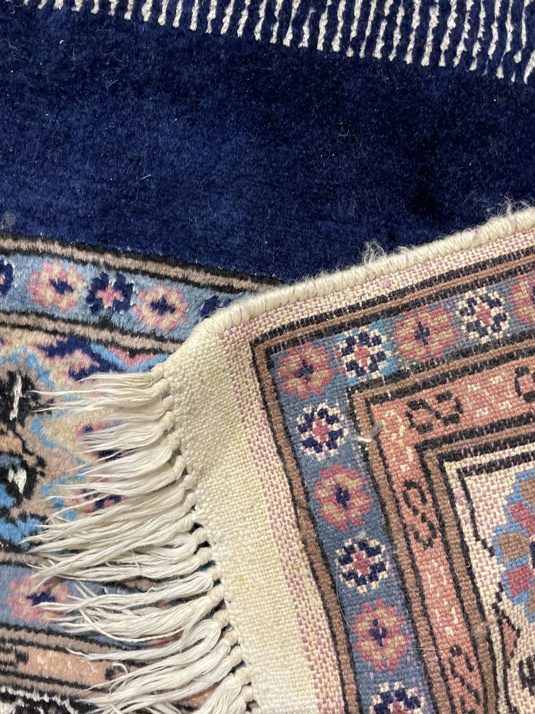 Indo-Persian indigo ground rug, the field depicting a rug with floral medallion and spandrels, enclosed within multiple floral pattern border bands
