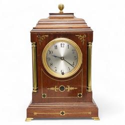 Edwardian- Early 20th century 8-day mahogany mantle clock, with a stepped pediment and brass finial, recessed brass pilasters and brass inlay to the front with a conforming plinth raised on bracket feet, silvered dial with Arabic numerals and steel spade hands within a glazed brass bezel, single train timepiece movement with pendulum and key.
