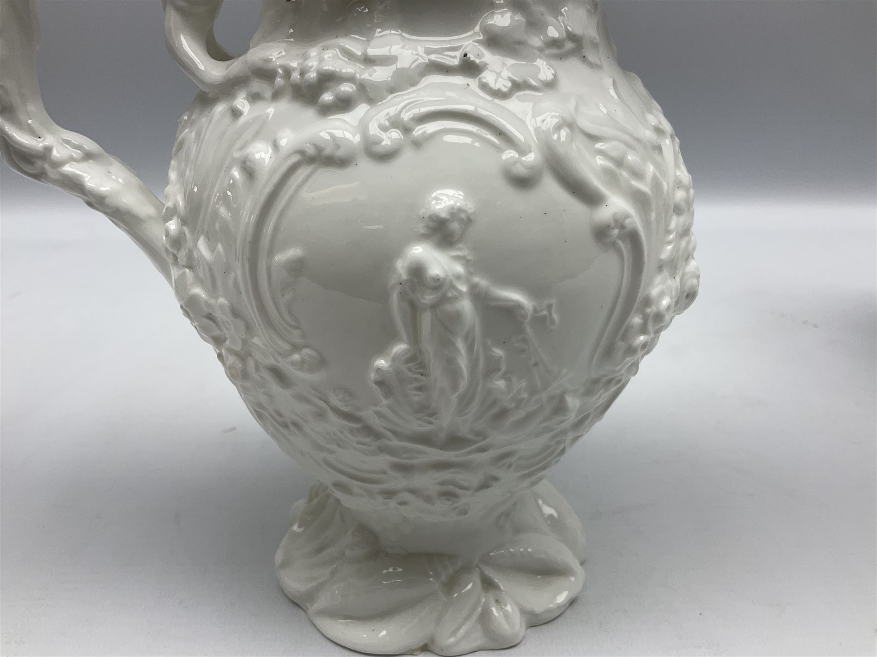 Pair of early/mid 19th century Copeland and Garrett white glazed pitchers, modelled in the Georgian style and moulded with the figures of Venus the Roman Goddess of Love, and Aurora the Roman Goddess of Dawn, within C scroll borders and foliate surround, the naturalistically modelled handle leading to a fruiting vine beneath the rim, upon a spreading base moulded with seashells, with printed green crowned wreath mark beneath, H20cm