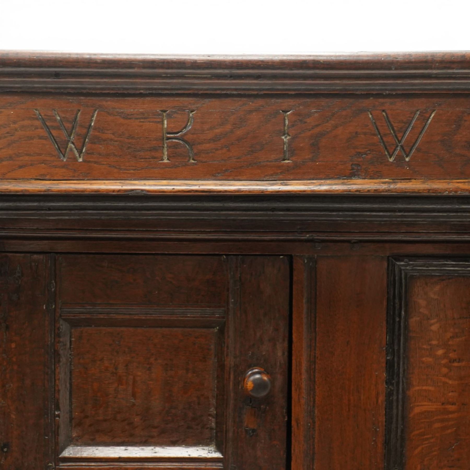 Early 18th century oak court cupboard, the projecting cornice carved with initials 'WKIW' and dated 1718 with turned terminals, fitted with two recessed panelled cupboard doors, large cupboard to base, raised on stile supports
