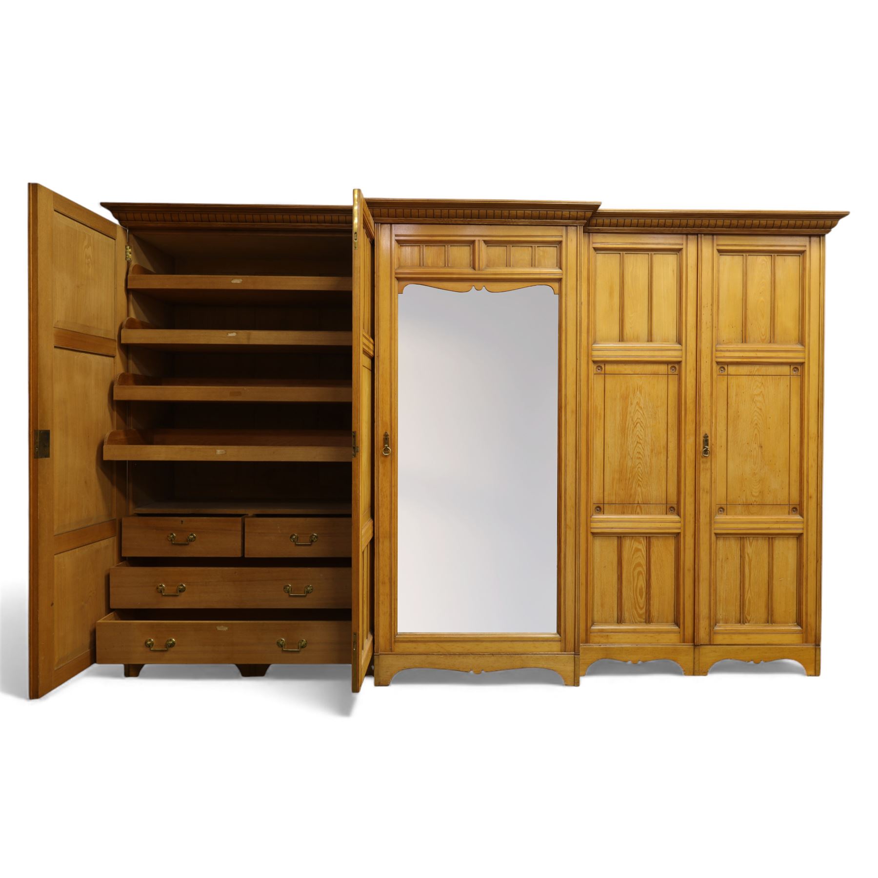 Gothic revival ash breakfront wardrobe in the manner of Charles Bevan, the four fielded panelled doors flanking a central mirrored door, opening to reveal an fitted interior with hanging rails and compartment shelves and drawers, upon a shaped plinth base with bracket cut feet

