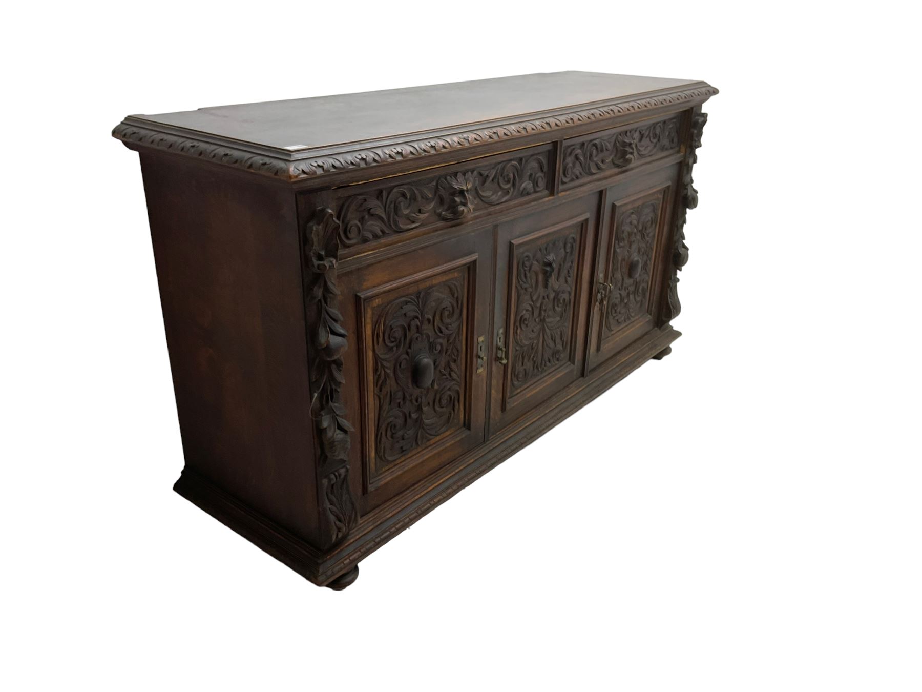 Victorian heavily carved oak sideboard, the moulded top carved with foliate decoration to the edge, fitted with two drawers and three cupboards, the drawer fronts carved with green man mask handles and scrolling foliage, the panelled doors carved with interlacing foliage, on turned compressed bun feet