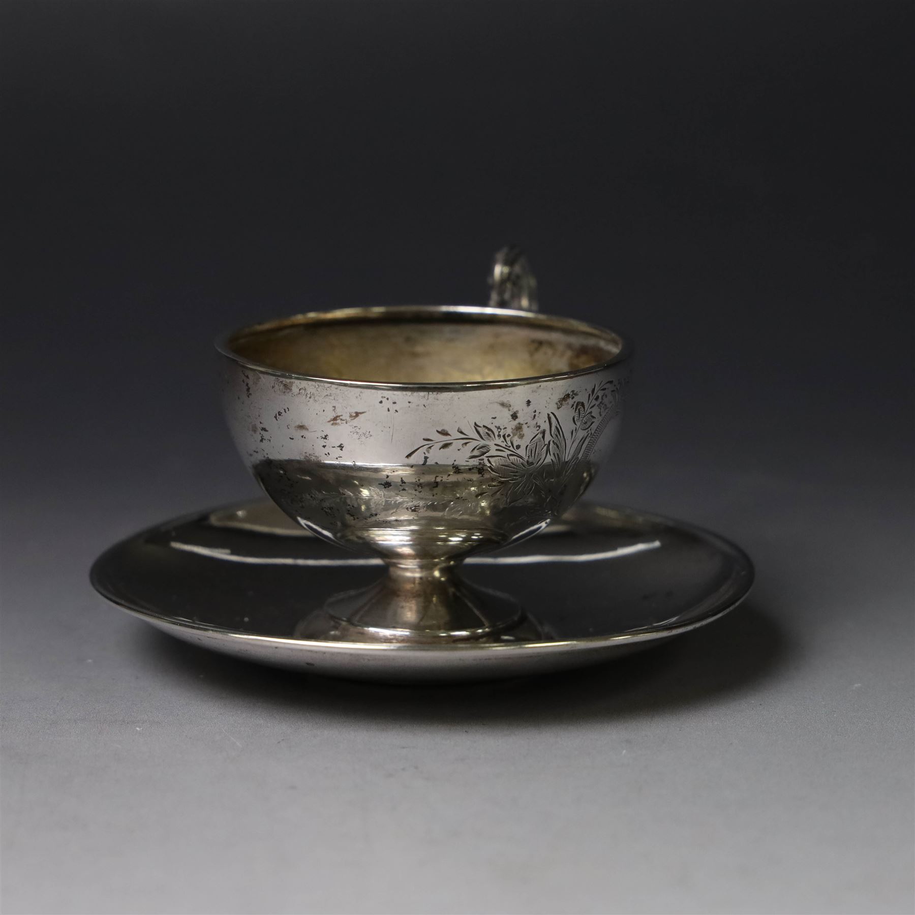 German silver cup and saucer, both with engraved foliate decoration, stamped 800, the saucer with crescent and crown mark