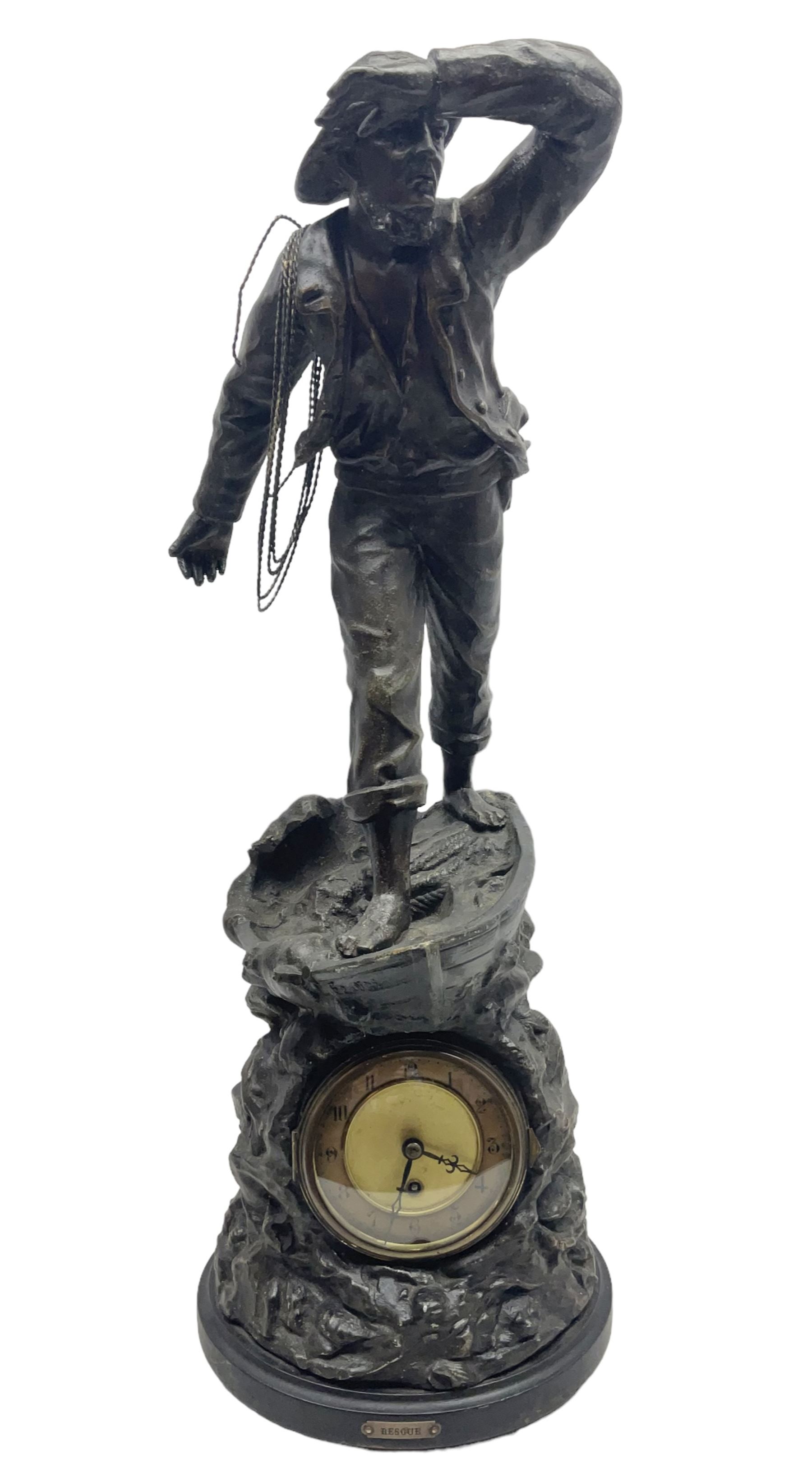 Early 20th century spelter effect figure of a sailor standing in the bow of a boat scanning the horizon, on a simulated rock base with a plaque entitled 'Rescue', base fitted with a timepiece clock movement and two-part dial, with pierced hands, gilt dial centre and ivorene chapter ring written in Arabic numerals, German HAC spring driven going barrel movement wound from the front; with pendulum H65.5cm
