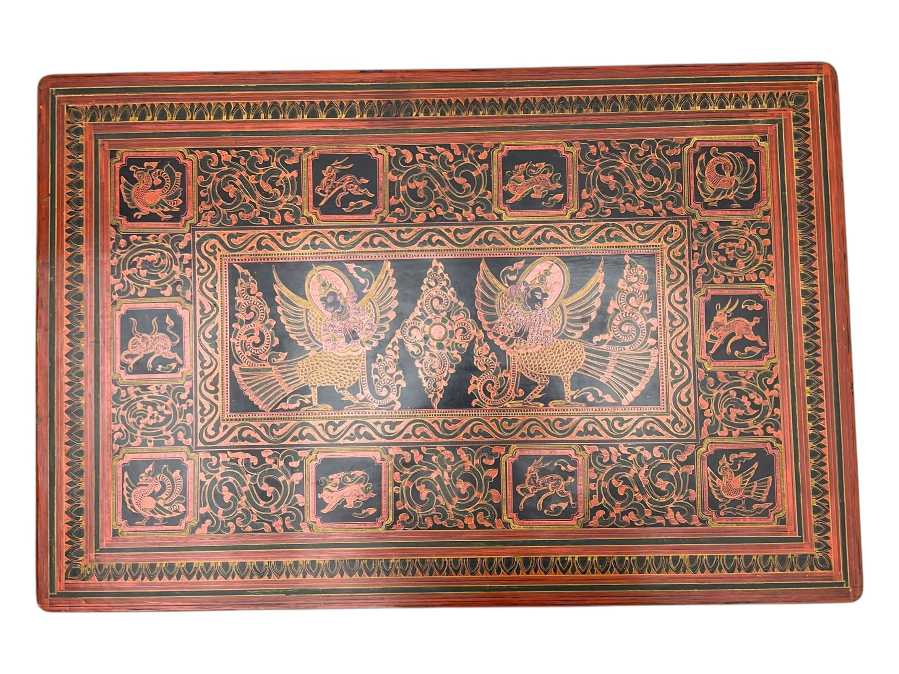 Late 20th century Burmese low table, the rectangular top and frieze decorated in traditional Shwezawa lacquer with gilded celestial figures, mythological beasts and dense foliate scrollwork, the folding base with hinged slab supports bearing conforming decoration