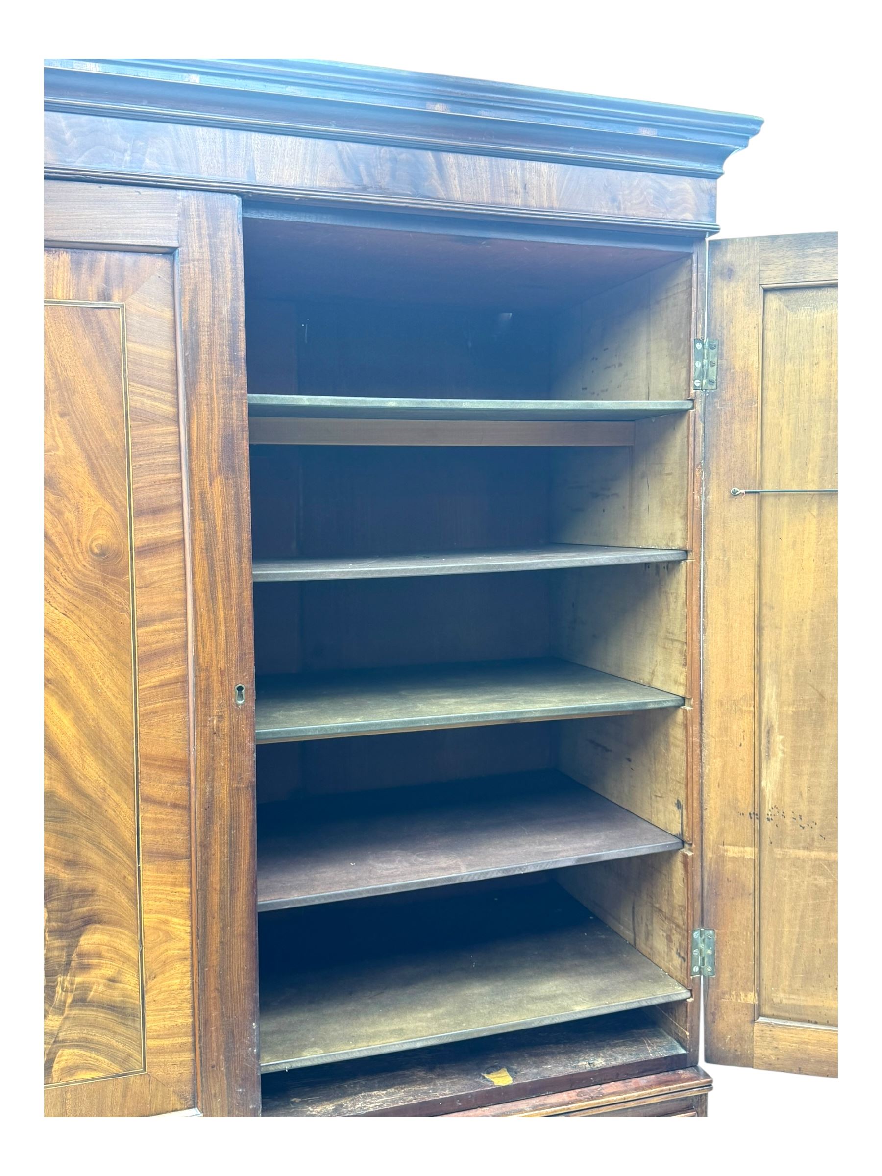 Early 19th century mahogany linen press cupboard, projecting moulded cornice over figured frieze, two panelled doors enclosing shelves, fitted with two short and two long cock-beaded drawers, on bracket feet 