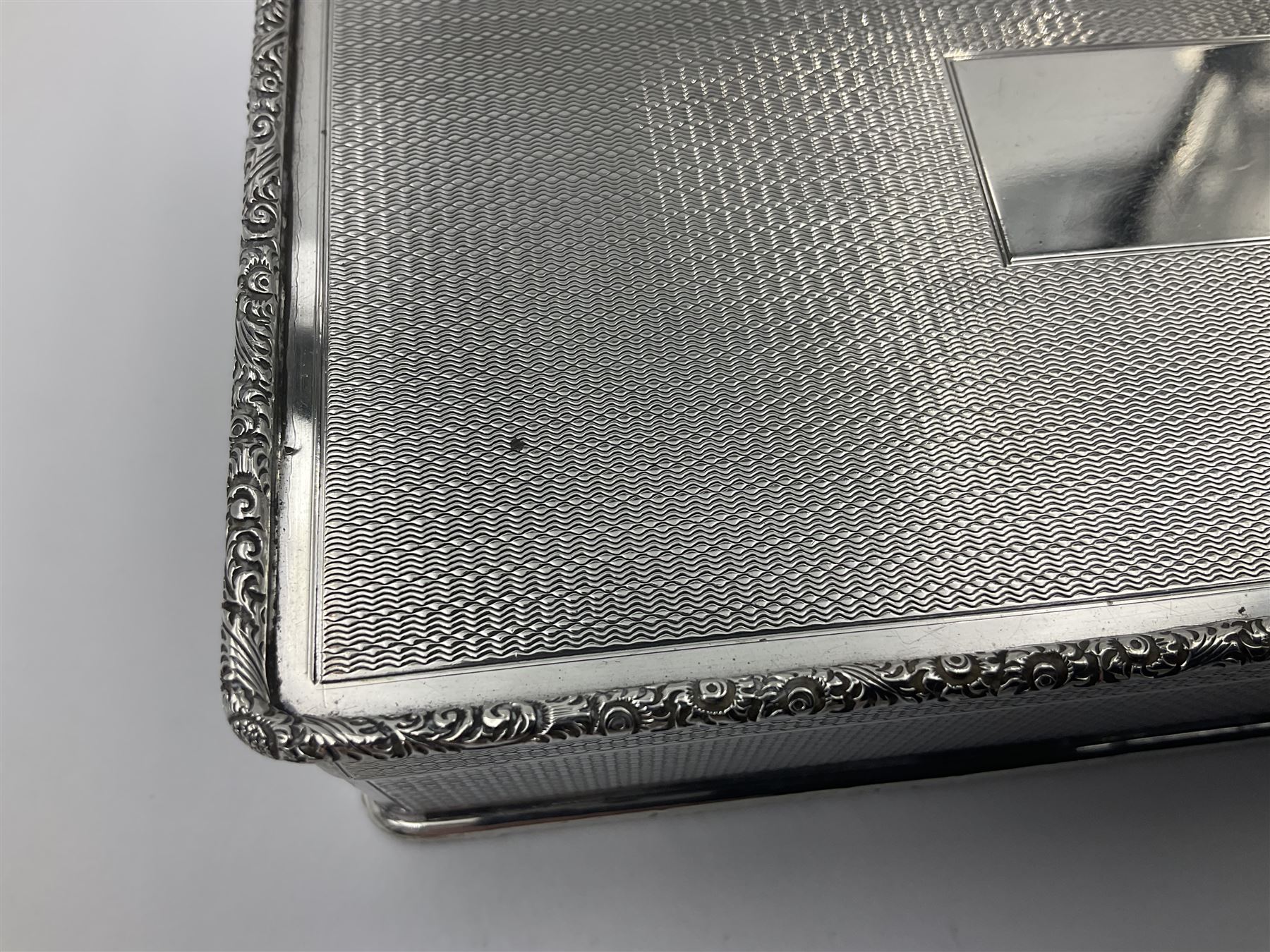 1920's silver table cigarette box, of rectangular form with engine turned decoration to the exterior, the hinged cover with central vacant rectangular panel and raised foliate rim, opening to reveal a gilt interior with later plush lining, hallmarked Charles Henry Dumenil, London 1923, H3.5cm L14.5cm D8.5cm