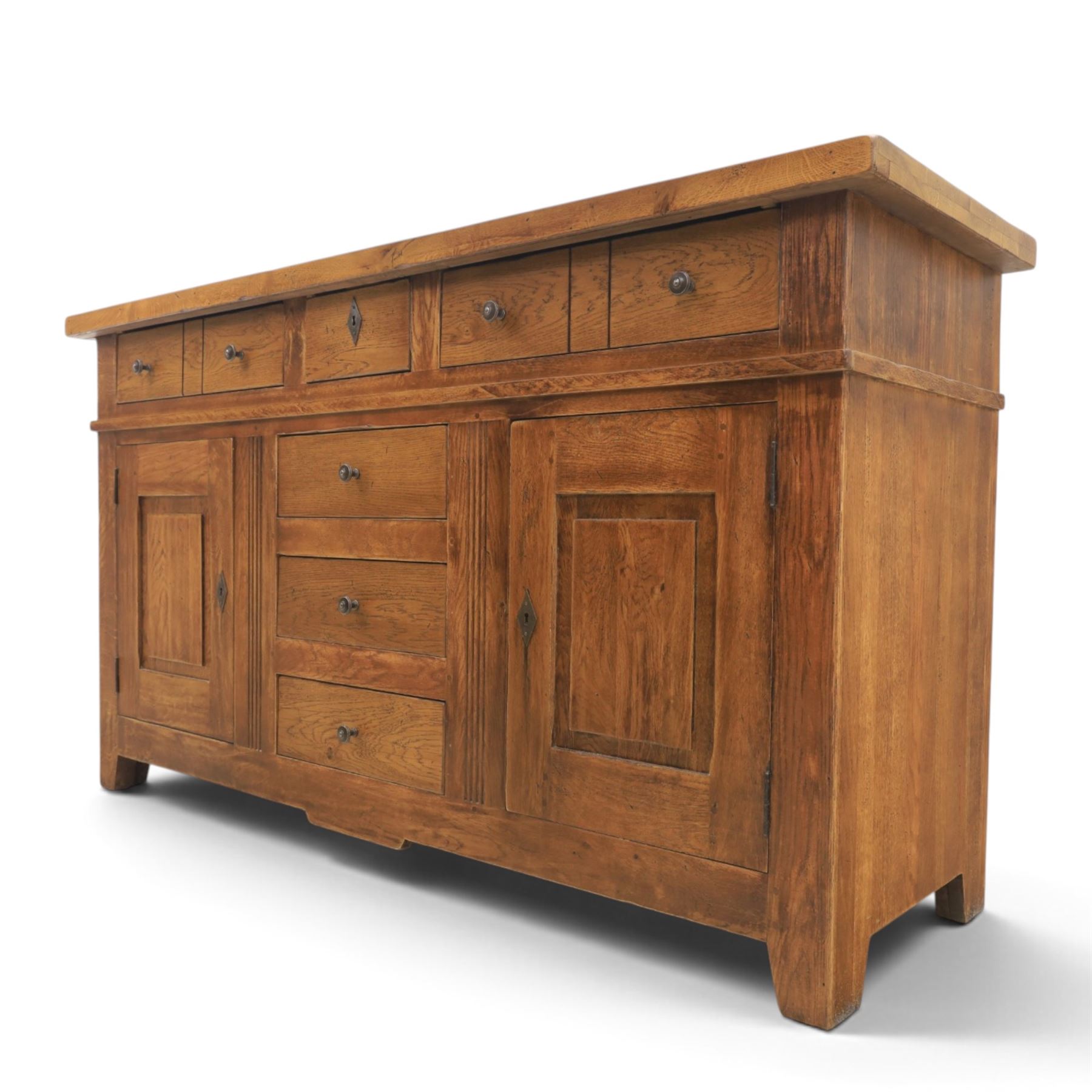 Indigo Furniture - large rustic oak sideboard fitted, with three drawers above three central drawers, flanked by fielded panelled doors, raised on bracket feet