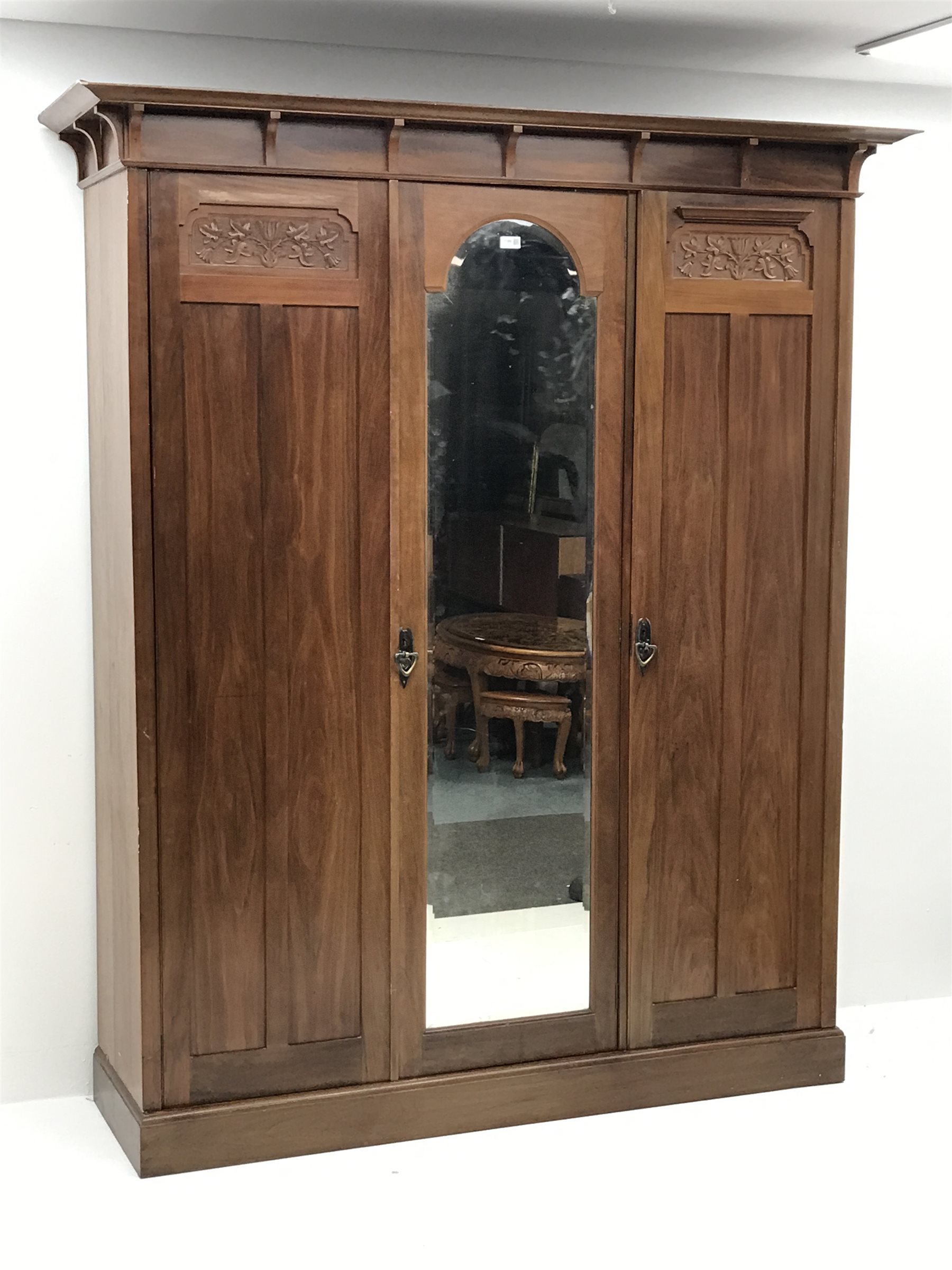 Irish Arts & Crafts walnut triple wardrobe circa 1908, projecting cornice above three doors enclosing fitted interior, single full length bevel edge mirror, platform base, W173cm, H204cm, D56cm