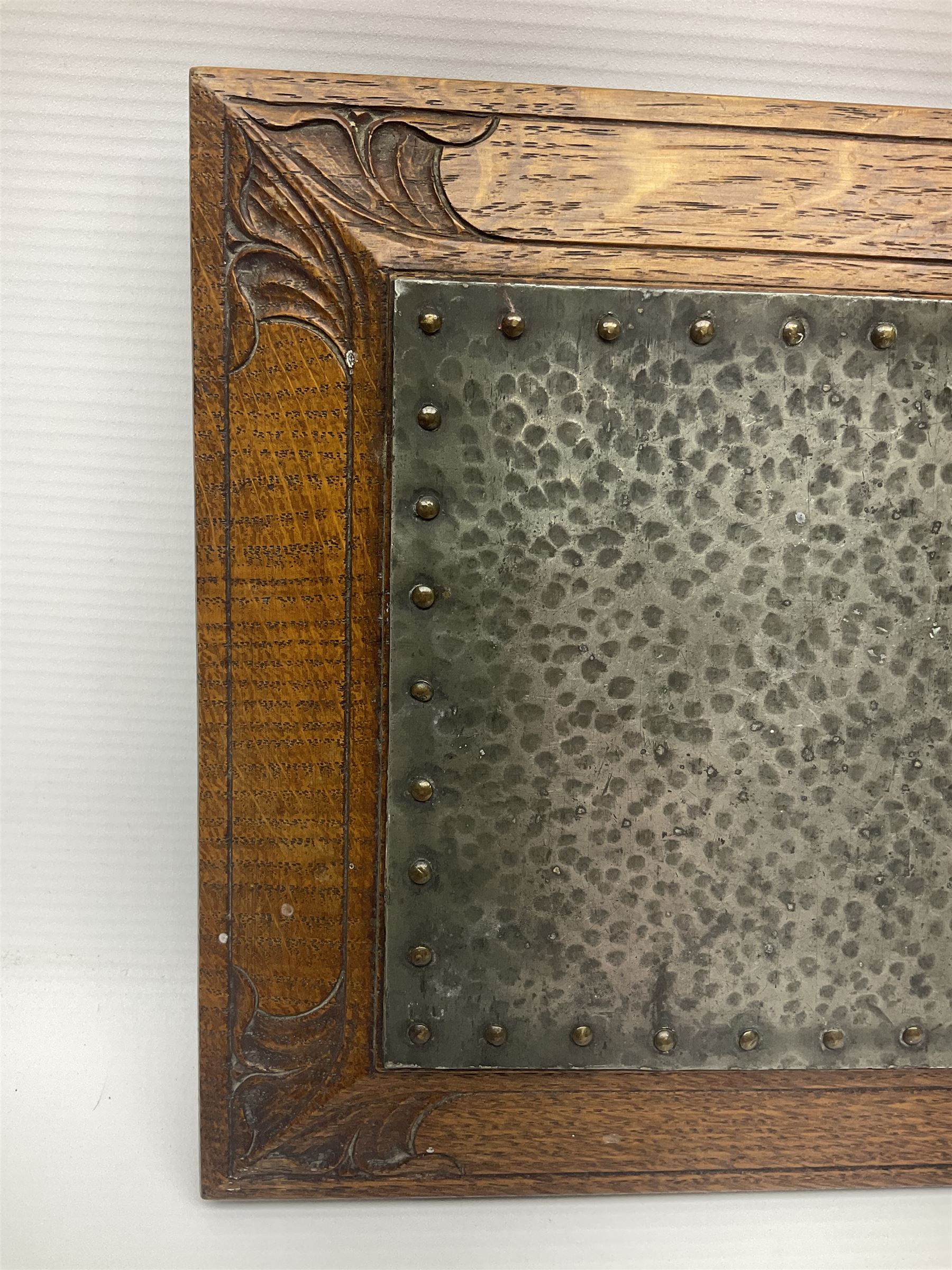 Arts and Crafts oak stand by Arthur Simpson of Kendal, of rectangular form with central hammered pewter panel, surrounded by a border with carved foliate corners, upon two bar supports, bearing label detailed 