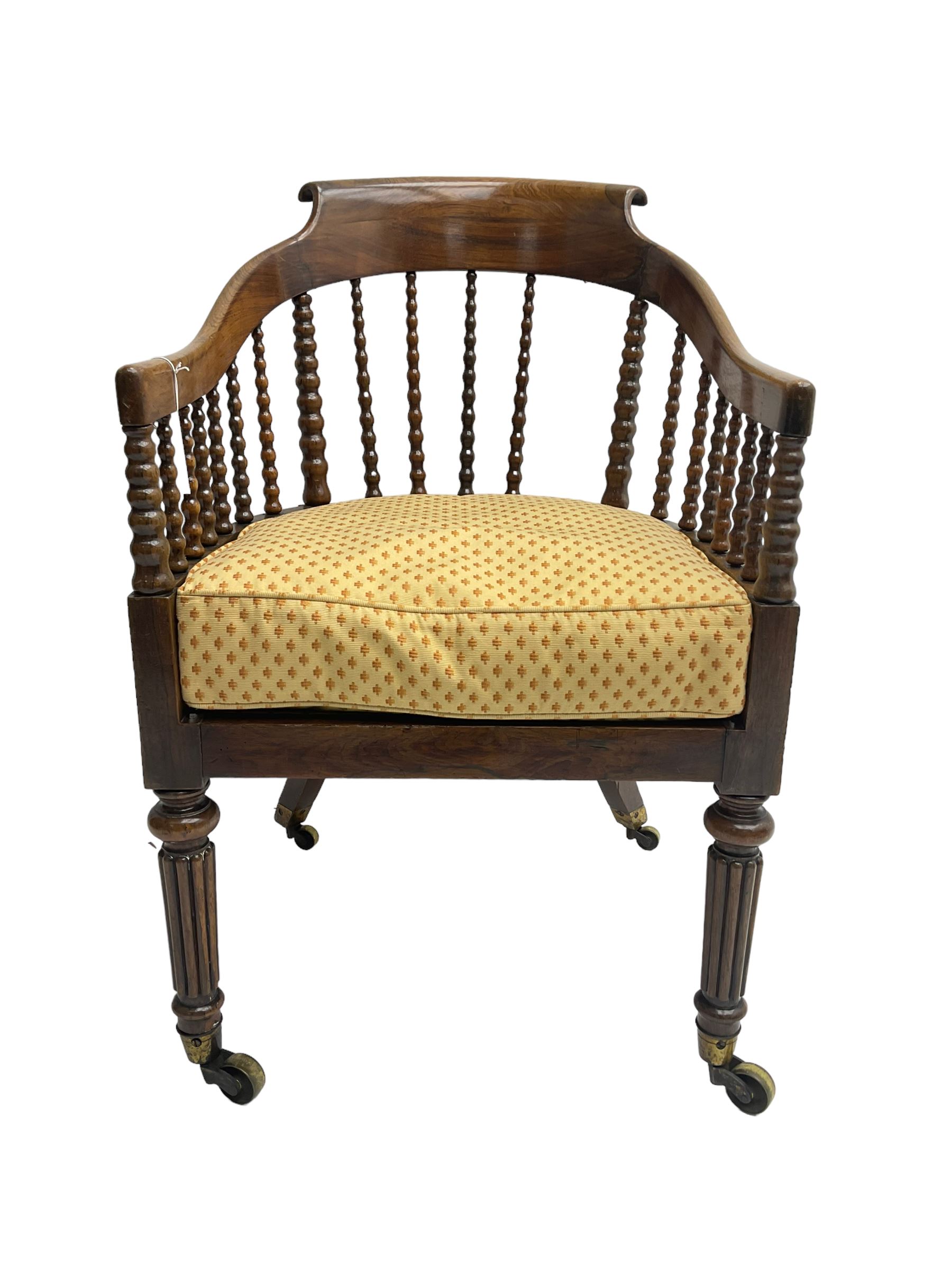 William IV rosewood tub armchair, the arched bow cresting rail over graduated bobbin turned spindles, cane seat with loose cushion, terminating in brass cups and castors.