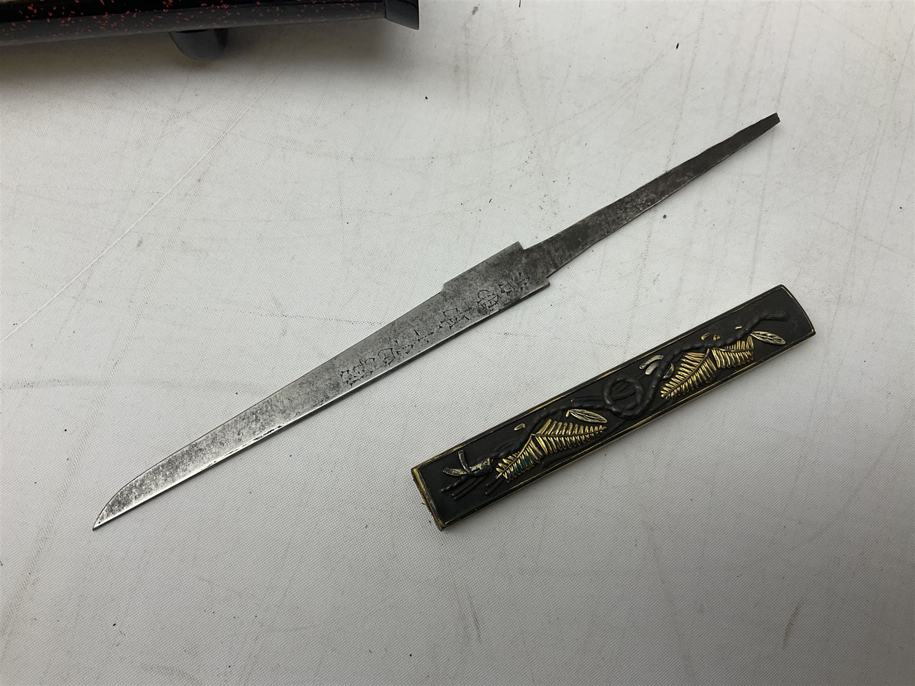 Japanese Tanto with 28.5cm steel blade and cord bound grip; in red spotted black lacquer saya containing a kogai knife with etched characters to the blade and ornate fern leaf and snake handle