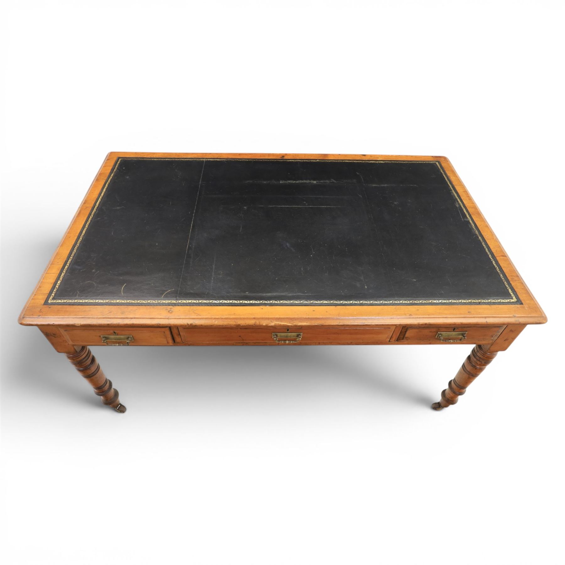 Victorian pitch pine writing table with leather inset top, rectangular top with three frieze drawers, pierced brass handles, raised on turned and fluted supports terminating in castors