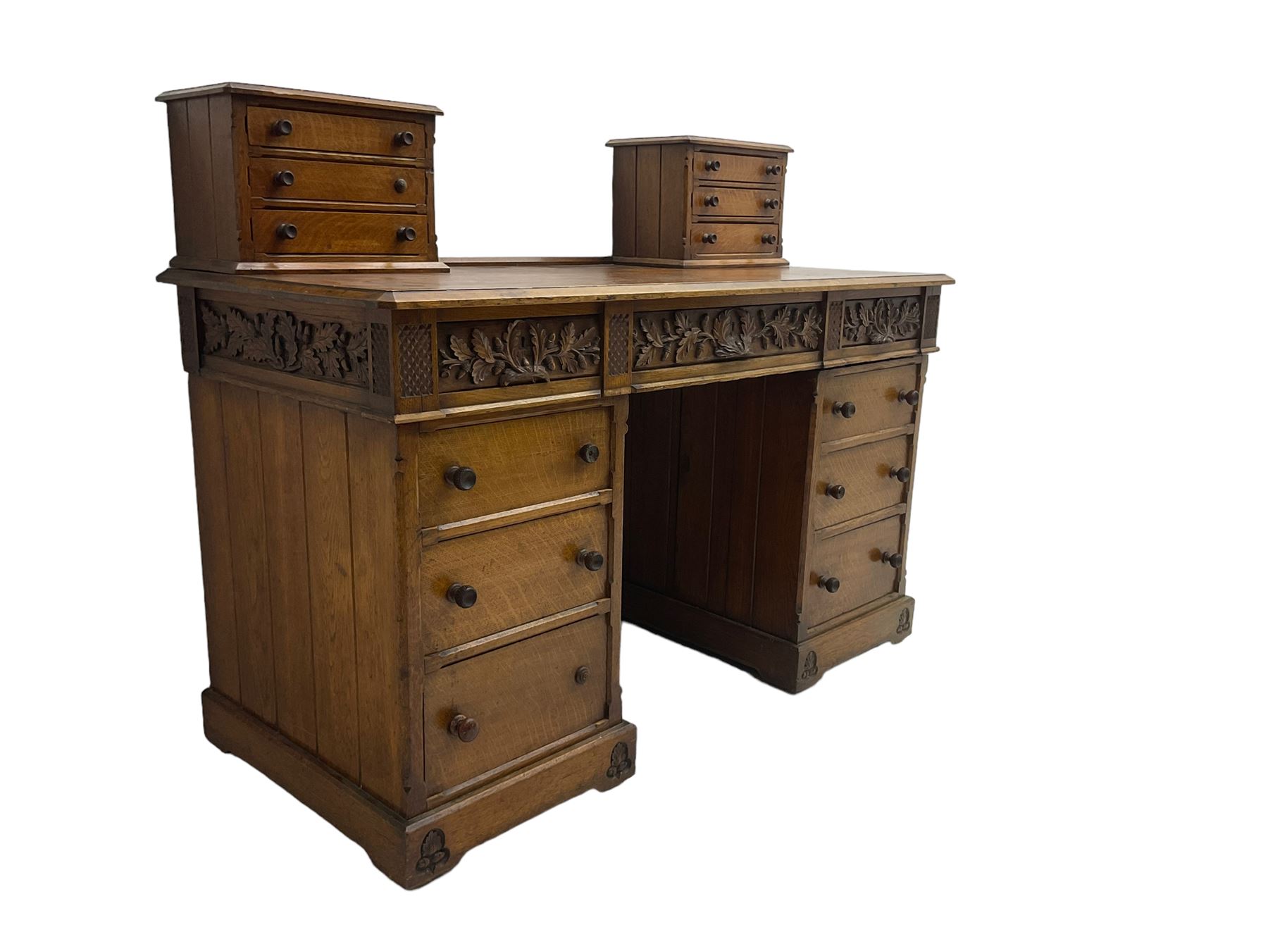 Late 19th century heavily carved oak twin pedestal desk, rectangular top with two raised trinket or correspondence structures each with three drawers, rectangular top over three frieze drawers carved with acorn and oak leaf decoration, each pedestal with three drawers with acorn husk shaped handles