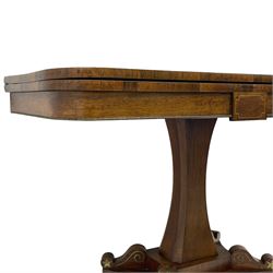 Regency rosewood and brass inlaid card table, the rectangular fold-over and swivelling top with rounded corners with a satinwood band, opening to reveal a blue baize lined interior playing surface, the frieze with a raised panel with satinwood stringing and a lower beaded brass edge, the concave and canted column with a shaped platform base applied with scrolls with brass star inlays and stringing, quadruple splayed supports terminating in foliate cast cups and castors