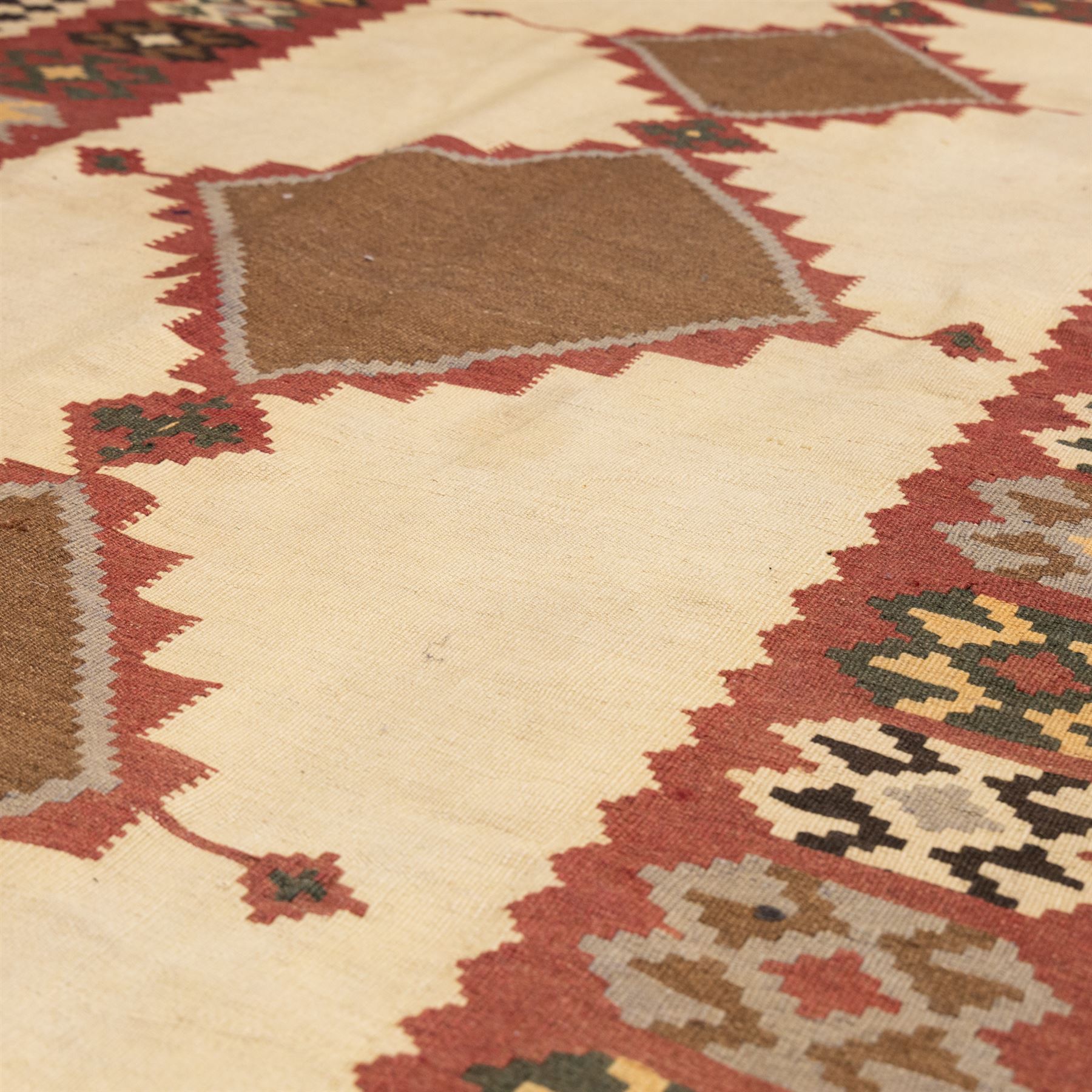 South West Persian Qashqai kilim, woven in flatweave in earthy tones, camel brown, ivory, olive, green, black, and madder red with three bold lozenge-shaped medallions, geometric borders incorporating stepped, hooked, and rosette motifs 