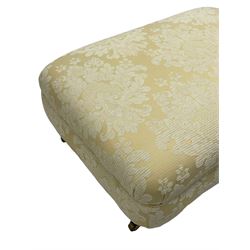 Rectangular hardwood-framed footstool, upholstered in pale gold and cream damask fabric with repeating foliate pattern, on turned feet with brass cups and castors