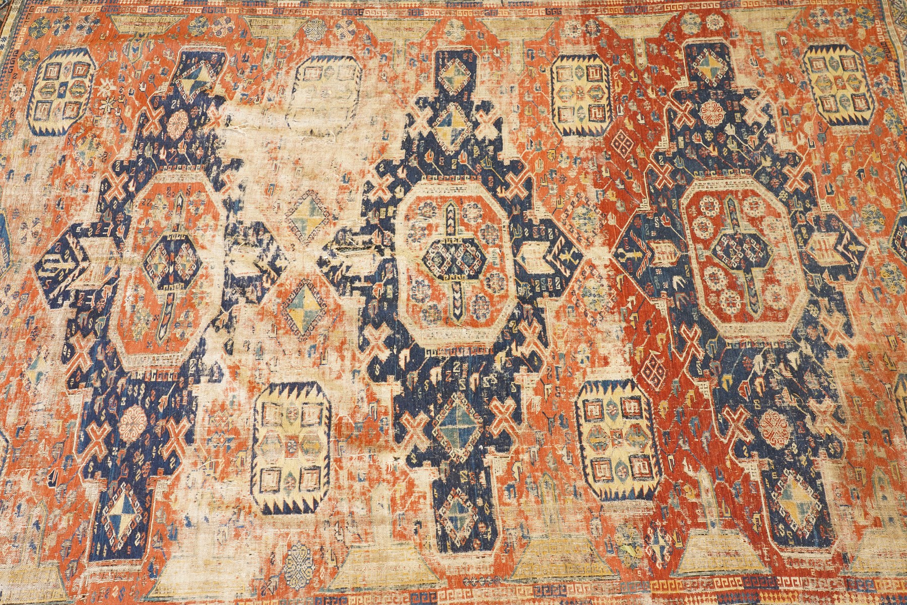 Antique Caucasian crimson ground carpet. the field decorated with three geometric indigo medallions with surrounding geometric motifs and guard lines
