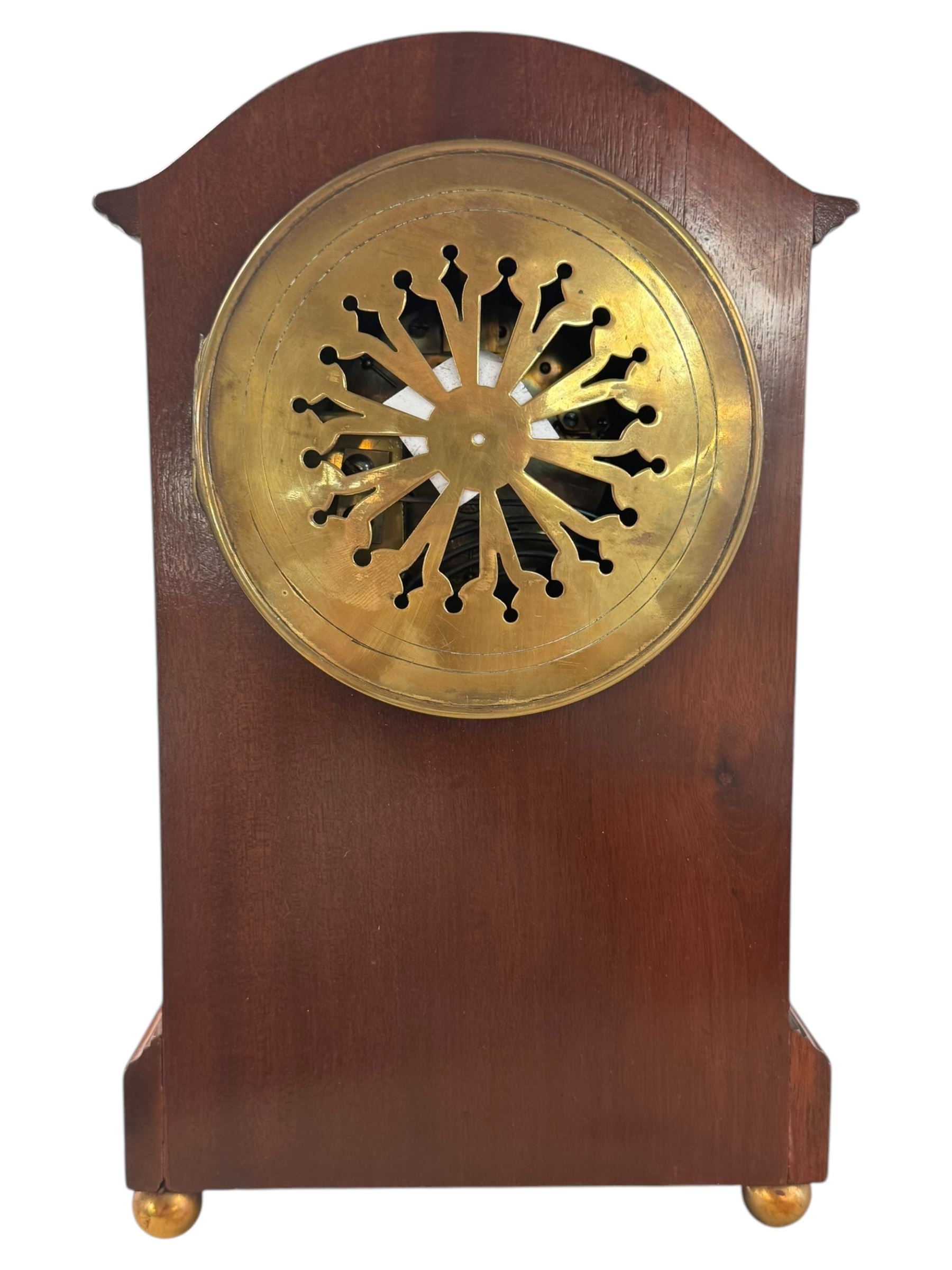 Edwardian-French 8-day mantle clock in a mahogany case with satinwood inlay, on a narrow plinth raised on ball feet, enamel dial with Roman numerals and steel moon hands, rack striking movement, sounding the hours and half hours on a gong. With pendulum and key.