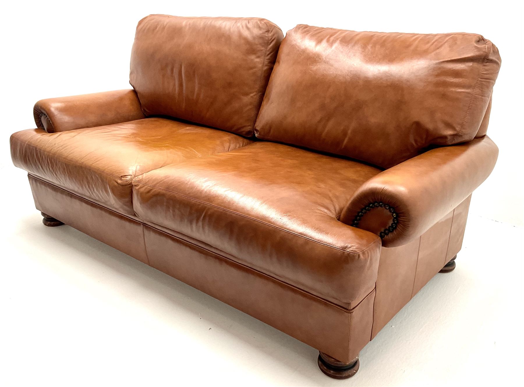 Three seat studded tan leather sofa, scrolling arms, turned supports (W190cm) with matching two seat (W155cm) armchair (W100cm) and footstool 