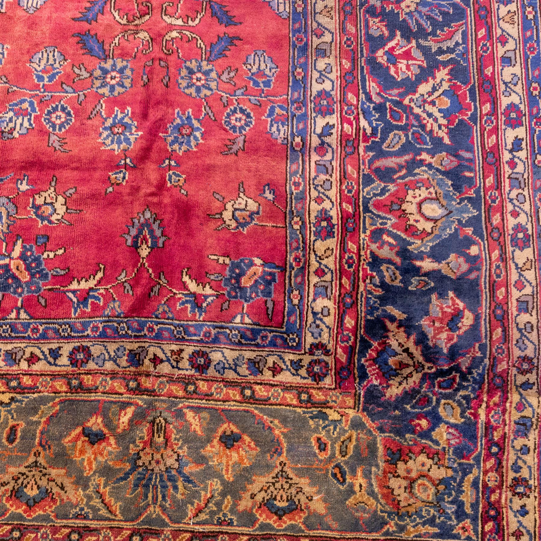 Large Persian-style mahal-type hand-knotted carpet, of rectangular form with a deep crimson field decorated with an all-over arrangement of stylized floral sprays and palmettes, with a central subtle medallion composition enclosed by a dark navy main border of scrolling floral motifs between narrow guard stripes with fringe ends 