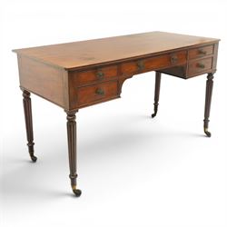 In the manner of Gillows - Regency period mahogany kneehole writing table, rectangular top over central cock-beaded frieze drawer with shaped spandrels, flanked by two graduating drawers to either side, raised on turned and fluted supports terminating to brass cups and castors