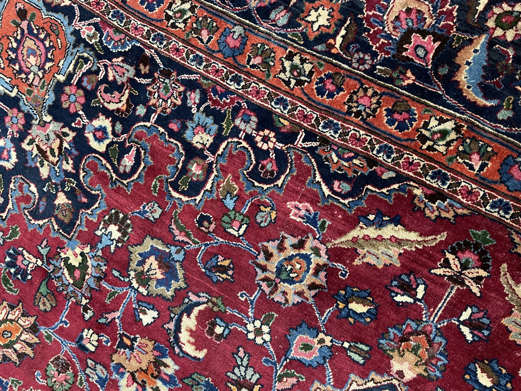 Persian Meshed carpet, plum ground and decorated with stylised flower heads and interlacing foliate, large central stylised medallion with orange detail, the orange mirrored in the five band border decorated with scrolling floral design, signature panel to end 