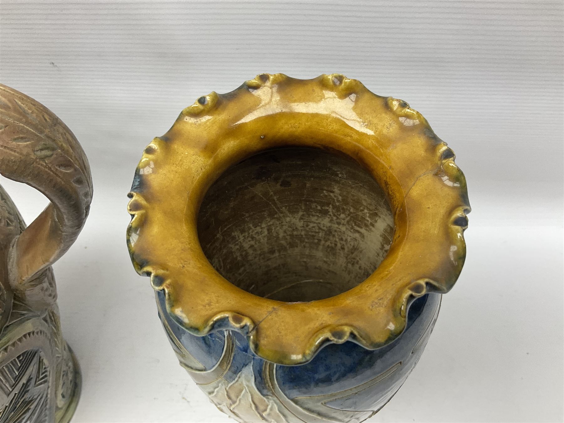 Early 20th century Royal Doulton stoneware vase, decorated with a stylized floral design below a wavy rim, monogrammed B.N, possibly for Bessie Newbery, H28cm, together with an early 20th century glazed jug, heavily carved throughout (2)