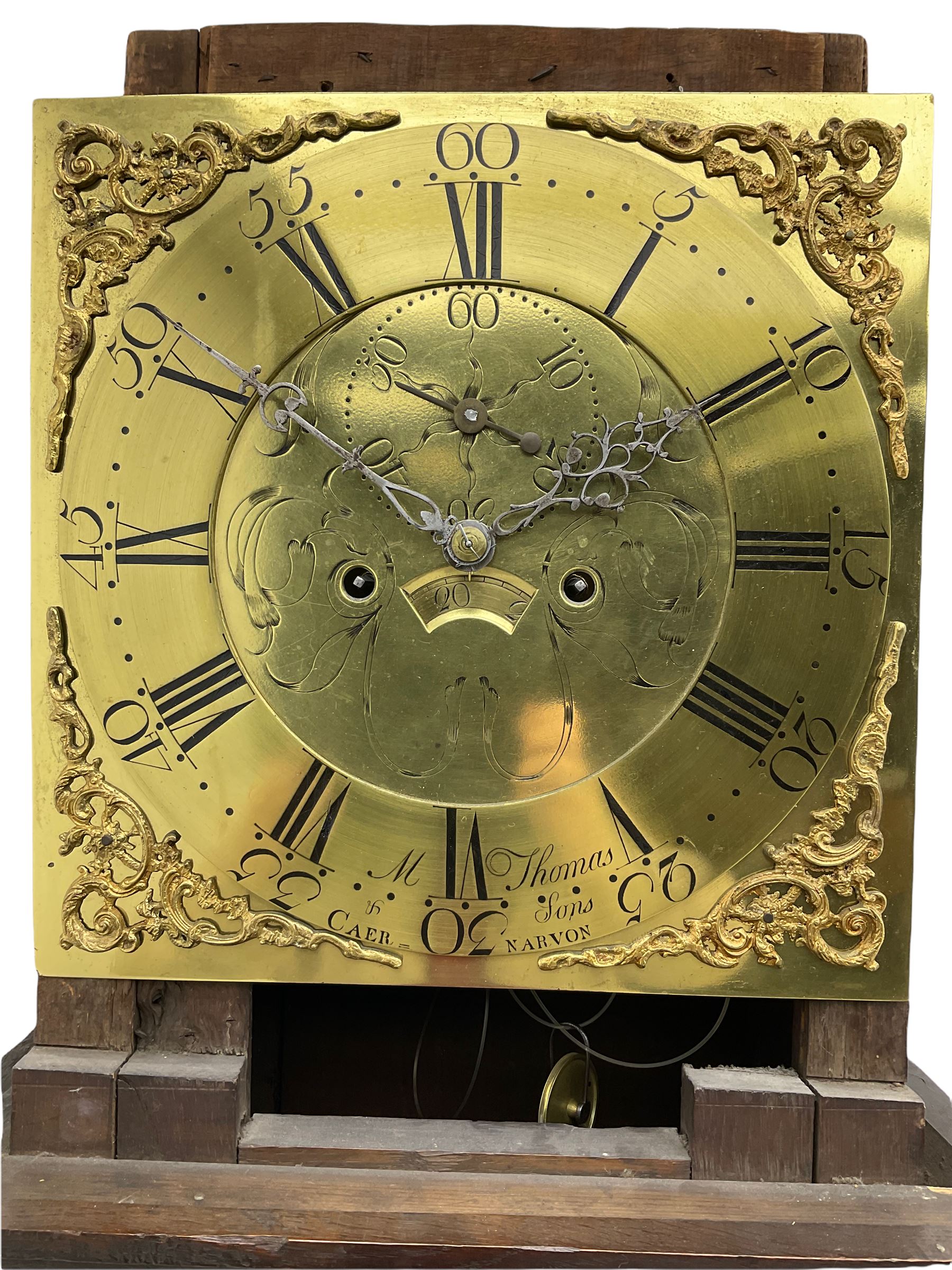 An 18th century oak cased longcase clock by M Thomas & Sons, Carnarvon c1780, flat topped hood with a wide cornice and plain frieze, glazed hood door flanked by two shaped pillars, with a long trunk and  door with a break arch top, with canted and reeded corners on a short plinth with a raised conforming break arch panel and skirting, 13” brass dial with an engraved centre,  small semi-circular date aperture and disc behind, with a subsidiary seconds dial, non-matching steel hands and scroll spandrels, Engraved chapter ring with roman numerals, five minute Arabic's and minute markers, dial pinned directly to an eight day rack striking movement, striking the hours on a cast bell. With weights, pendulum and key.    
Michael and Morris Thomas are recorded as working together in Carnarvon 1769-94.




