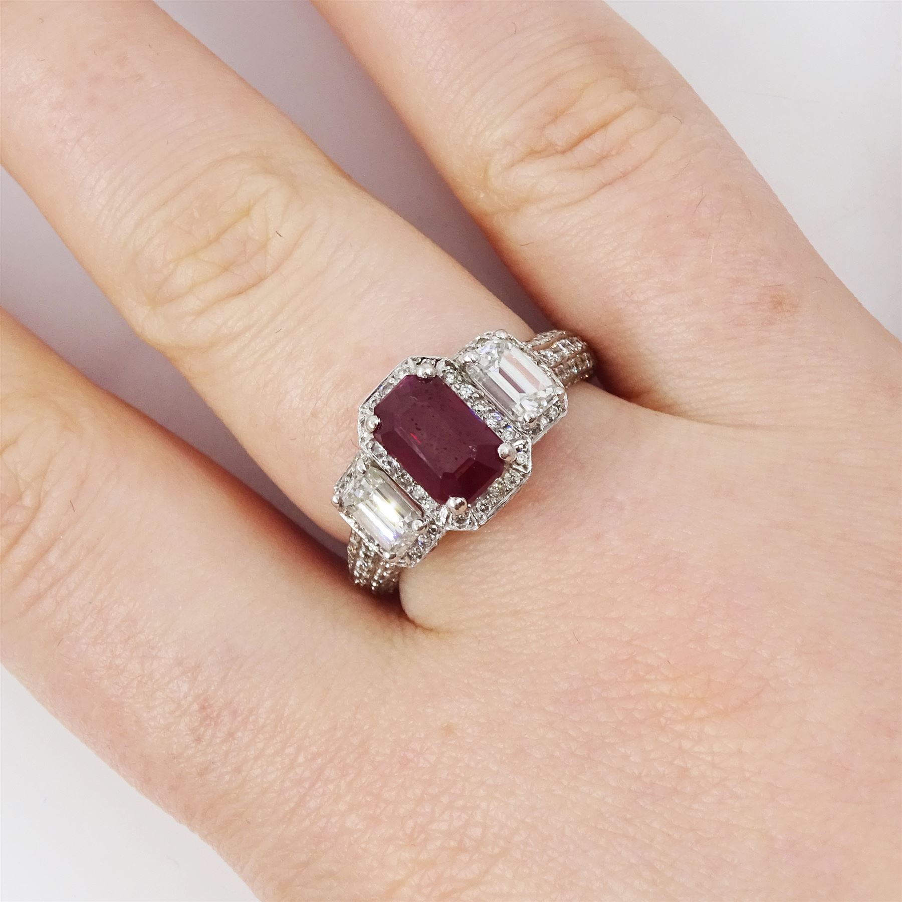 18ct white gold ruby and diamond trilogy ring, single emerald cut ruby of approx 1.85 carat, with a single emerald cut diamond set either side, all surrounded by round brilliant cut diamonds, the shoulders set with three rows of round brilliant cut diamonds, principal two emerald cut diamonds approx 1.10 carat