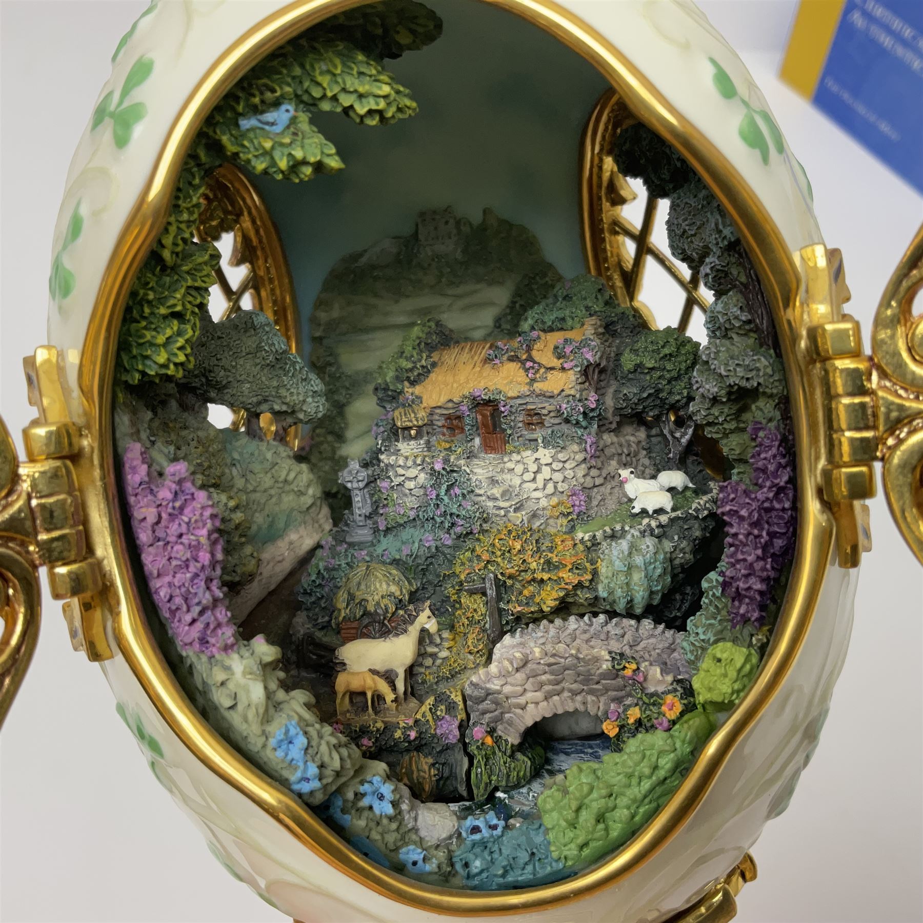Franklin Mint The Emerald Isle Collector Egg, the egg decorated with embossed shamrocks upon a cream ground, with a gilded shamrock finial, accents and openwork door, opening to reveal a miniature landscape scene, upon three gilded feet set with green paste stones, with certificate of authenticity H23cm, 