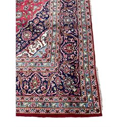 Central Persian Kashan crimson ground carpet, central  floral pole medallion with matching spandrels within a field of scrolling palmette motifs and foliage, the heavily banded indigo border with repeating plant motifs interlaced with scrolled branches