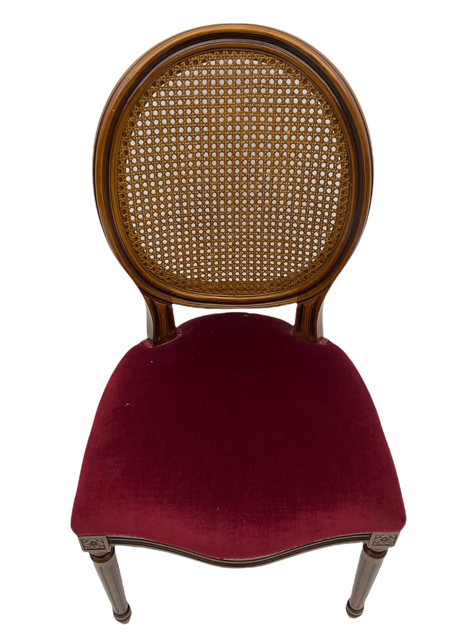 Set six French style walnut finish dining chairs, oval cane bergere backs over serpentine seats upholstered in red, flower head carved fluted supports