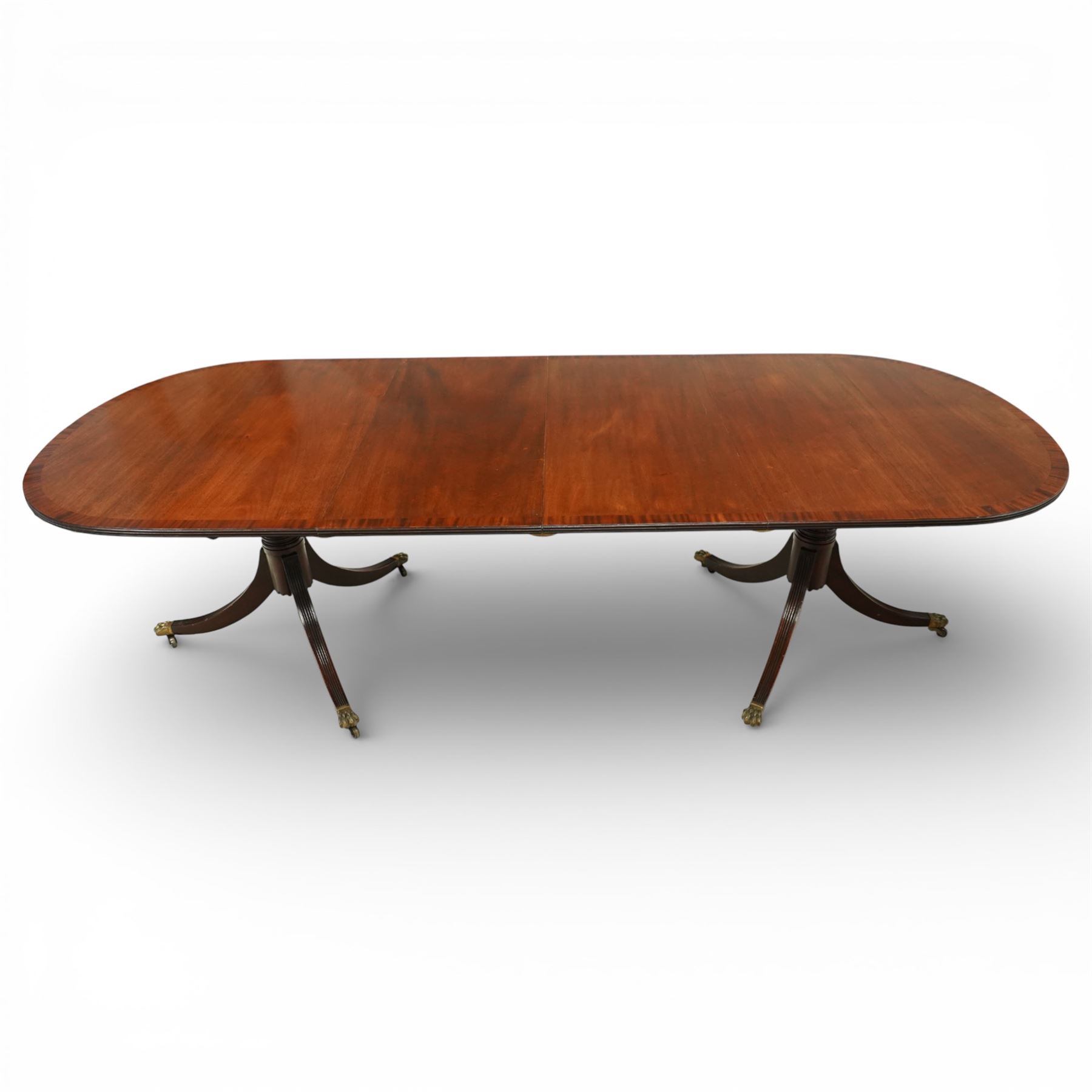 Arthur Brett & Sons - Regency design mahogany extending dining table and eight chairs, the oval top with rounded ends and two extension leaves, raised on twin pedestal supports with swept legs terminating in brass caps and castors, accompanied by a set of eight chairs comprising six single chairs and a pair of carvers, the chairs with curved backs and horizontal splat rails, upholstered seats, sabre legs and scrolling arms to the carvers
(Extends to 252cm)
(Chairs H 86cm, W 52cm)