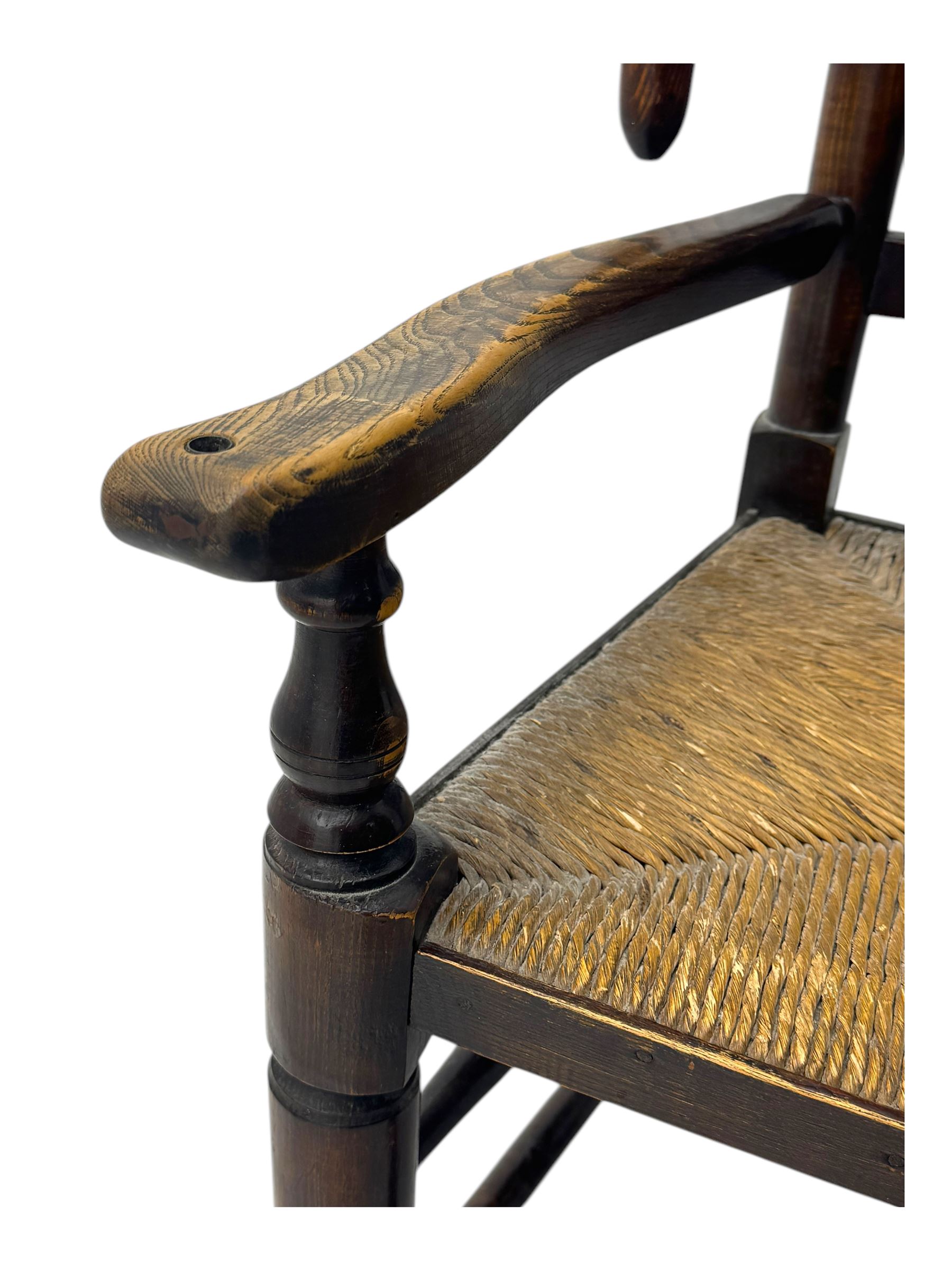 Early 19th century ash armchair, the back with winged spindles extending from a shaped top rail, above a splat of two rows of vertical spindles, with curved arms and a rush seat, raised on turned supports united by double stretchers terminating in castors