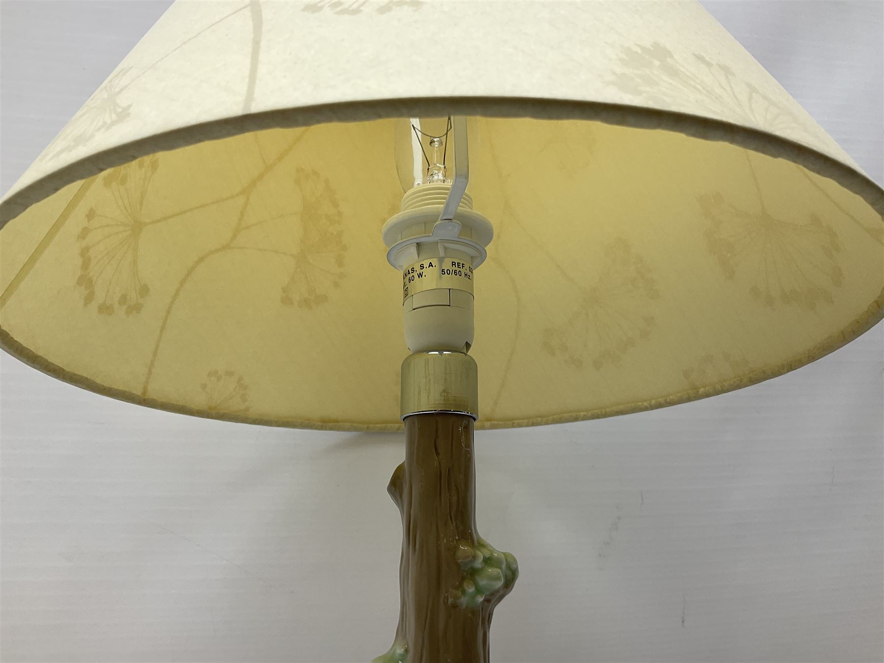 Nao table lamp modelled as a boy playing the flute upon logs with two recumbent sheep at his feet, the stem modelled as a tree trunk, with fabric shade, with printed mark beneath, H46cm