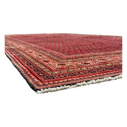 Persian Arak crimson ground rug, the field decorated with repeating Boteh motifs within geometric guard stripes