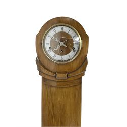 English - 1930s light-oak cased 8-day grandmother clock, in a stylised case with a long trunk on raised feet, with a matching wooden dial centre and a silvered chapter with Roman numerals, three train Westminster chiming Garrard movement chiming the quarters and hours on 8 gong rods. With a lever platform escapement.